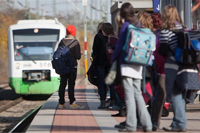 Schüler stehen an einem Bahnsteig, während ein Zug einfährt.