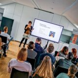 Dr. Stefanie Marzian vom Verein Herausforderung steht beim Info-Tag „Wellenbrecher“ vor einem Raum voller Menschen und hält einen Vortrag.