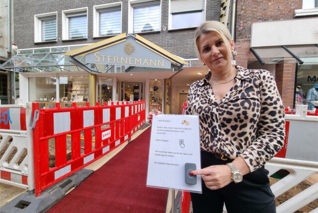 Eine Frau steht vor einer Baustelle und drückt eine Klingel.