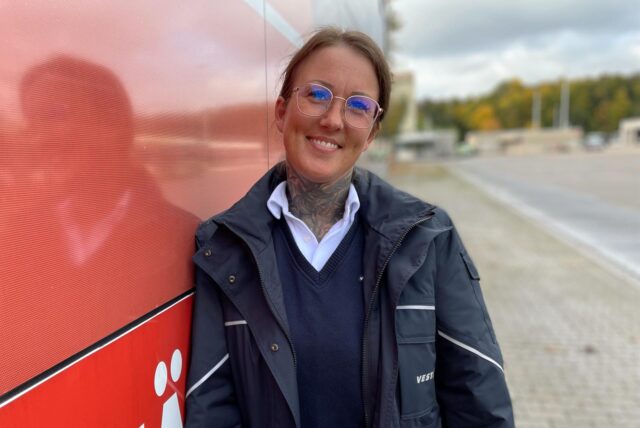 Aylin Schiller in blauem Busfahrer-Blouson lehnt entspannt lächelnd an einem Bus der Vestischen.