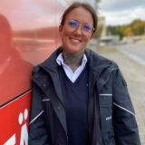 Aylin Schiller in blauem Busfahrer-Blouson lehnt entspannt lächelnd an einem Bus der Vestischen.