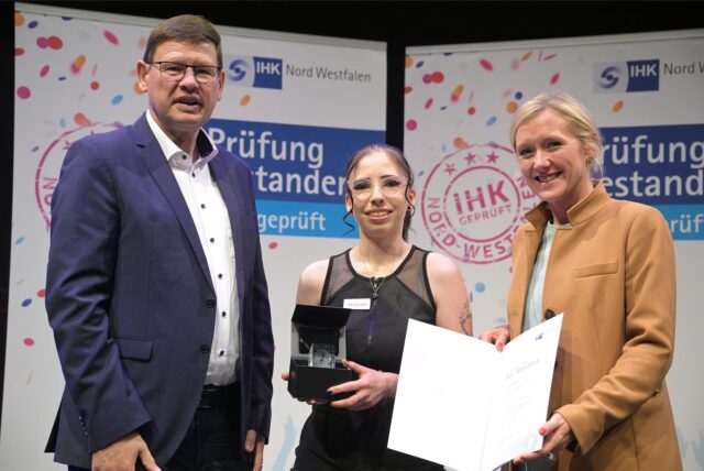Jochen Grütters, Hannah Bafs und Melanie Baum stehen nebeneinander. Hannah Bafs trägt eine kleine Glas-Trophäe, Melanie Baum präsentiert Bafs‘ Urkunde.