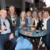 Eine Gruppe von Männern und Frauen sitzt und steht bei letzten  Feierabendmarkt des Jahres 2024 in Herten-Langenbochum an einem Tisch.
