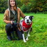 Eine Frau kniet auf einer Wiese im Hertener Schlosspark neben einem Hund.