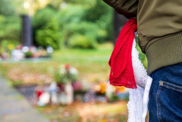 Eine Person, aus dessen Jacke Damenunterwäsche ragt, läuft auf dem Waldfriedhof in Herten an einer Reihe von Gräbern vorbei.