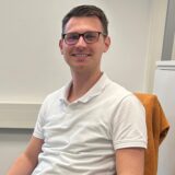 Robin Gude sitzt an seinem Schreibtisch, vor ihm zwei große Bildschirme.