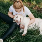 Hundefutter Rückruf: Foto einer kaukasischen Frau, die ihren Golden Retriever umarmt, der im Gras liegt.
