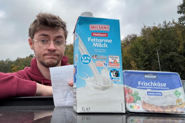 Vincent Rastfeld lehnt auf ein Autodach. Vor ihm auf dem Dach steht eine Packung Fettarme Haltbare Milch und eine Packung Frischkäse. Rastfeld hält einen Kassenzettel in die Kamera und und zieht eine Augenbraue hoch.