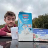 Vincent Rastfeld lehnt auf ein Autodach. Vor ihm auf dem Dach steht eine Packung Fettarme Haltbare Milch und eine Packung Frischkäse. Rastfeld hält einen Kassenzettel in die Kamera und und zieht eine Augenbraue hoch.