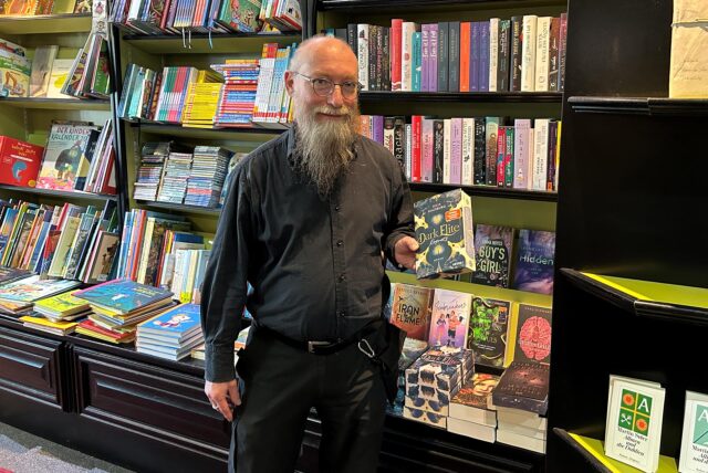 Wolfgang Tänzer steht im Bücherwurm vor Bücherregalen und hält ein Buch mit mehrfarbigem Farbschnitt in der Hand.
