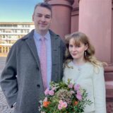 Das junge Ehepaar Glen und Vivian steht, nach ihrer Standesamtlichen Trauung auf dem Rathausplatz in Dortmund. Im Hintergrund sieht man die Säulen des Standesamts.