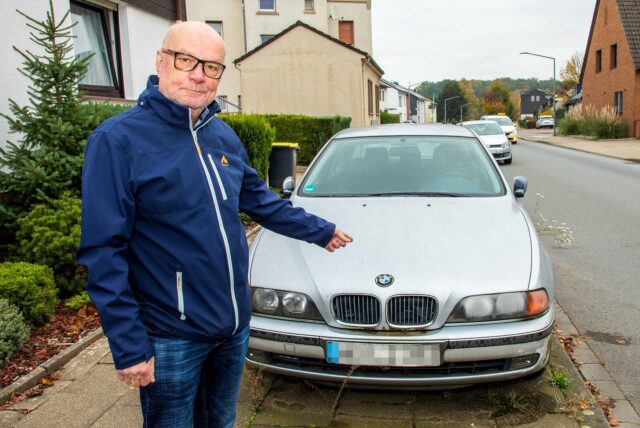 Ein Mann zeigt mit seinem Finger auf einen silberfarbenen BMW auf dem Gehweg der Uhlandstraße in Herten.