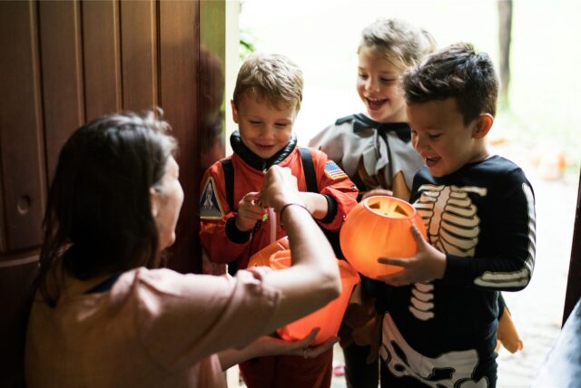 Mit dem richtigen Halloween-Spruch bekommen diese drei verkleideten Kinder von einer Frau Süßigkeiten überreicht.