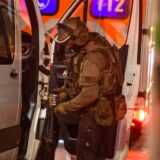 Eine Person in SEK Kleidung steht an der Tür eines silbernen Vans und hantiert an einer Waffe.