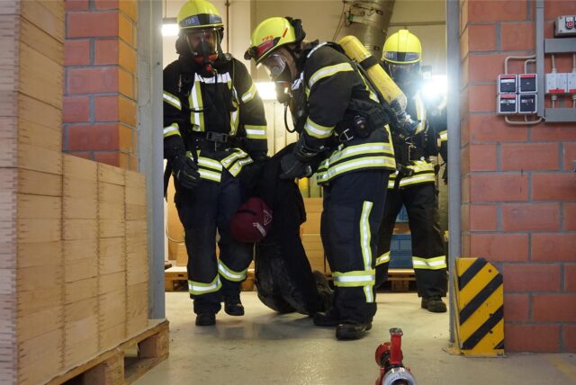 Feuerwehrleute schleppen eine hilflose Person aus einem Haus.