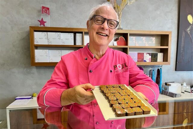 Manfred Glatzel steht in der Schokoladen-Manufraktur Pott au Chocolat in Dortmund und hält ein Tablett mit Pralinen in den Händen.