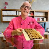 Manfred Glatzel steht in der Schokoladen-Manufraktur Pott au Chocolat in Dortmund und hält ein Tablett mit Pralinen in den Händen.