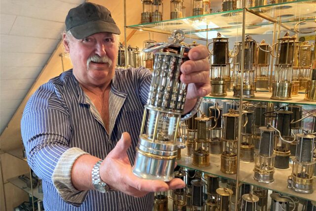 Wolfgang Dudek steht mit in einer Grubenlampe in der Hand vor einer Vitrine mit vielen weiteren.