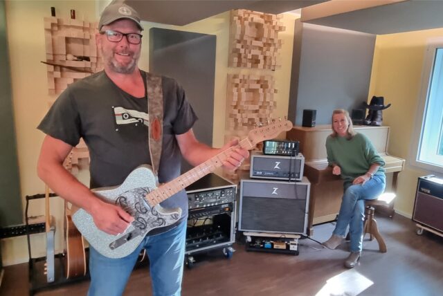 Marcell Müller steht mit einer Gitarre im neuen Tonstudio in Recklinghausen, während Tina Müller am Klavier sitzt.