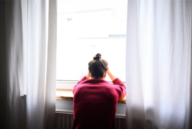 Eine Frau sitzt mit Kopf in den Händen am Fenster.