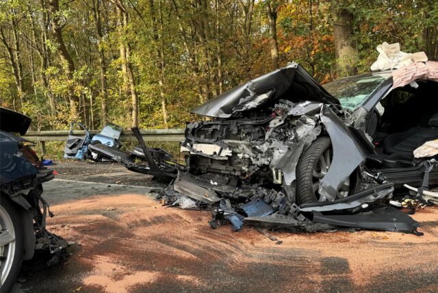 Zwei Autos mit stark zerstörten und eingedrückten Fronten stehen sich auf einer Straße an einem Waldweg gegenüber.