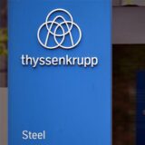 Das Thyssenkrupp-Logo steht vor einer Werksanlage.