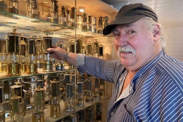 Wolfgang Dudek aus Marl greift nach einer Grubenlampe, die mit vielen weiteren in einer Vitrine ausgestellt ist.