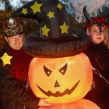 Zwei kostümierte Menschen stehen an Halloween neben einem beleuchteten Kürbis, der einen Hexenhut trägt.