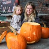 Kristina Mertin, eine junge Frau, sitzt gemeinsam mit ihrem Kind vor einem Tisch, auf dem Kürbisse liegen. Einer von den Halloweenkürbissen, hat ein geschnitztes Gesicht.