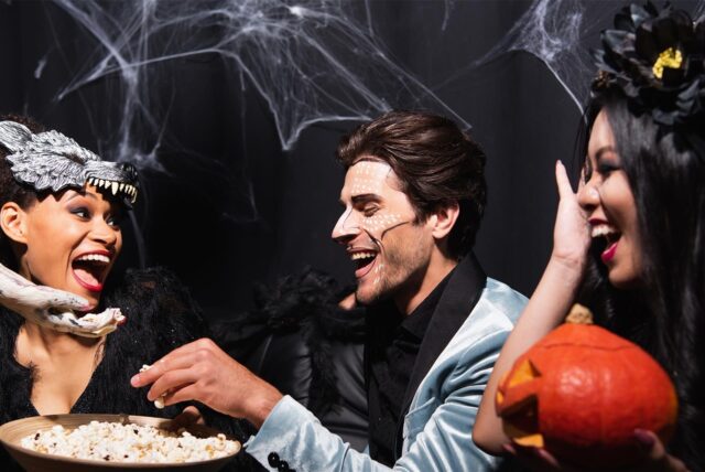 Drei verkleidete Partygäste teilen sich Popcorn auf einer Halloweenfeier.