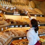 Eine Frau nimmt in einer Bäckerei einen Laib Brot aus der Auslage.
