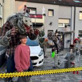 Jonas Pohnke steht vor einer überlebensgroßen Werwolf-Figur im Vorgarten seines Familienhauses. Im Hintergrund ist ein Auto geparkt. Daneben sind mehrere Halloween-Deko-Figuren aufgestellt. Mehrere Skellte, ein Kürbis-Kopf und Spinnenweben. Am Balkon ist ein Plakat mit „Happy Halloween“ aufgehängt.