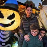 Eine Frau und zwei kleinere Kinder stehen zwischen einer Halloween-Kürbis-Puppe und einem kleinen Skelett.
