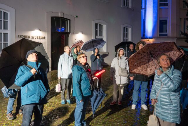 Mehrere Personen mit Regenschirm schauen in den Nachthimmel.