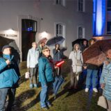 Mehrere Personen mit Regenschirm schauen in den Nachthimmel.