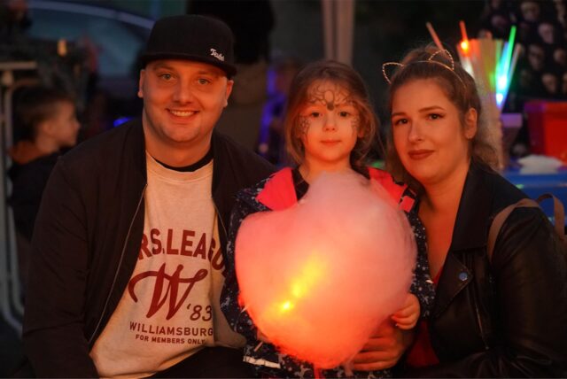 Eine verkleidete Familie lächelt in die Kamera. Das Mädchen hält Zuckerwatte in den Händen.