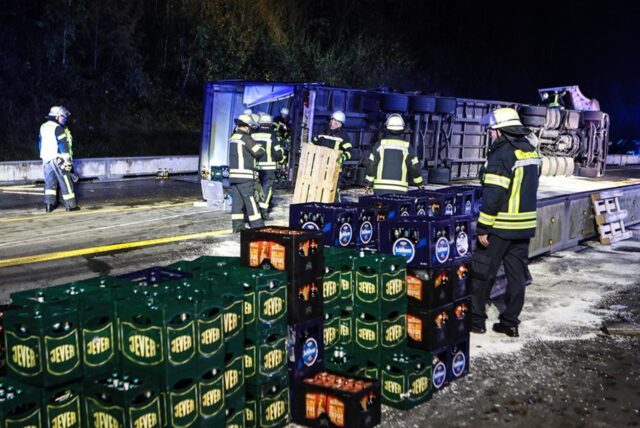 Der Laster liegt im Hintergrund auf der Seite, Bierkästen stapeln sich neben Feuerwehrkräften.