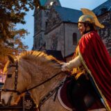 Katrin Zobel reitet als Sankt Martina auf einem Pferd durch das Alte Dorf Westerholt in Herten. Im Hintergrund ist die St.Martinus-Kirche zu sehen.