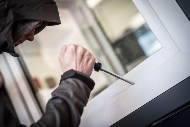 Ein Mann mit Kapuze über dem Kopf versucht, ein Fenster mit einem Schraubendreher zu öffnen.