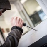 Ein Mann mit Kapuze über dem Kopf versucht, ein Fenster mit einem Schraubendreher zu öffnen.