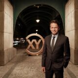 Moderator Rudi Cerne steht vor einer Unterführung, in der das Logo der ZDF-Sendung „Aktenzeichen XY … ungelöst“ zu sehen ist.