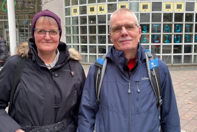 Das Ehepaar Kentschke steht vor dem Glashaus in Herten. Im Hintergrund sind die Luftballon-Buchstaben der Stadtbibliothek zu sehen. Beide tragen eine Jacke und lächeln in die Kamera.