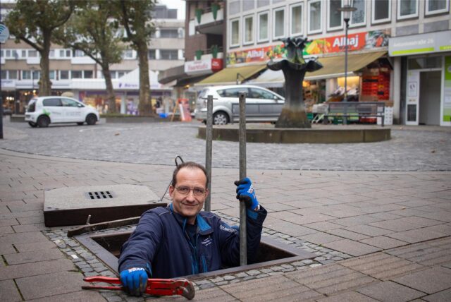 Thorsten Raschke ragt halb aus einem Abwasserkanal hervor, im Hintergrund ist der Brunnen an der Kranzplatte zu sehen.
