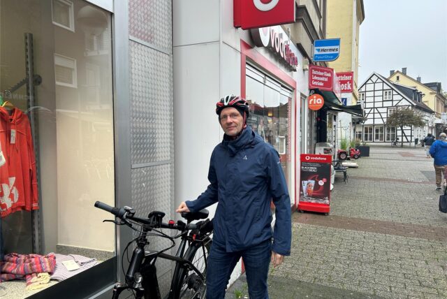 Ein Mann mit Fahrradhelm stützt sich mit der rechten Hand auf seinem Fahrradsattel ab. Er steht in der Innenstadt von Datteln.