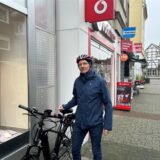 Ein Mann mit Fahrradhelm stützt sich mit der rechten Hand auf seinem Fahrradsattel ab. Er steht in der Innenstadt von Datteln.