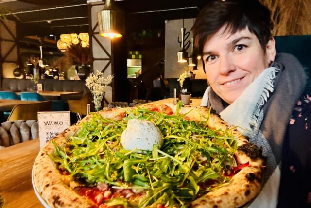 Redakteurin Jessica Will mit einer Pizza, belegt mit viel Rucola und Burratta.