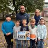 Anne Kemper, Sven Krambeer und fünf Schüler der Marktschule Ickern nehmen den Scheck des Lensing-Media-Hilfswerkens entgegen