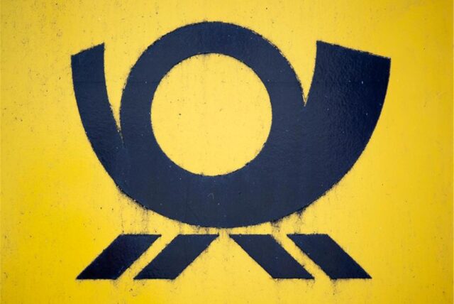 Blick auf einen Briefkasten der Deutschen Post, auf dem das Posthorn-Logo zu sehen ist.