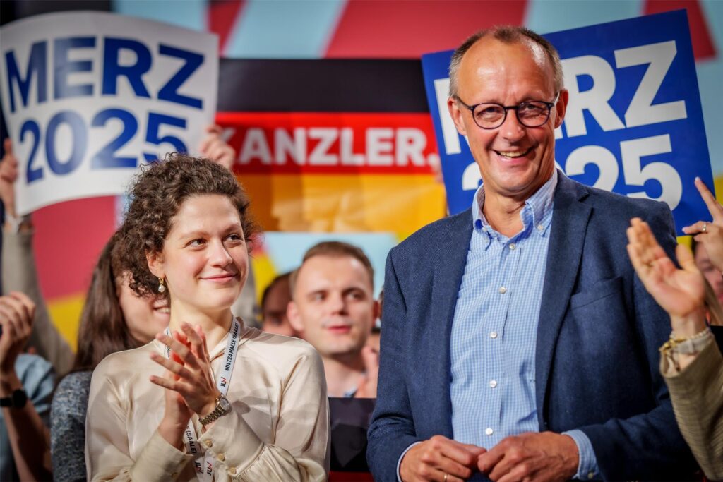 Sarah Beckhoff steht beim Deutschlandtag der Jungen Union neben CDU-Kanzlerkandidat Friedrich Merz, klatscht und lächelt ihm zu. Friedrich Merz lacht vergnügt in die Menge. Sarah Beckhoff steht beim Deutschlandtag der Jungen Union neben CDU-Kanzlerkandidat Friedrich Merz, klatscht und lächelt ihm zu. Friedrich Merz lacht vergnügt in die Menge.