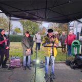 Ein Mann mit einem Mikrofon in der Hand steht neben einer Menschengruppe.